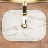 A top-down view of a white marble sink with gold fixtures, placed on a wooden surface. Produktbild-Vorschau