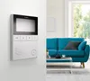 A video intercom system mounted on a wall next to a living room with a blue sofa. Produktbild-Vorschau