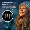 A young girl in winter clothing looking up at falling snow, with a circular inset showing icicle lights. Náhled obrázku produktu