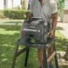 A person is holding a Ninja Woodfire Pro XL electric grill outdoors in a grassy yard. Voir les images du produit