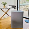A laundry basket and ironing board are set up in a room with a window overlooking a garden. Produktbild-Vorschau