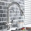 A kitchen faucet with a pull-down sprayer is shown in use, with water flowing from both the main spout and a secondary filtered water spout. Náhľad obrázku produktu