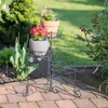 A metal plant stand with three tiers holding potted plants on a brick patio. Náhľad obrázku produktu