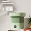 A light green and green collapsible washing machine is displayed on a countertop with a vase of pink tulips in the background. Náhled obrázku produktu