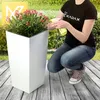 A person is tending to a plant in a white planter on a wooden deck. Anteprima dell’immagine prodotto