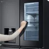 A hand is opening the glass door of a refrigerator, revealing the interior shelves and drawers. Produktbild-Vorschau