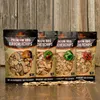 Four bags of premium BBQ smoking chips are displayed on a wooden surface in front of a wooden plank wall. Produktbild-Vorschau