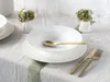 A table setting with white plates, gold cutlery, and small floral arrangements. Produktbild-Vorschau