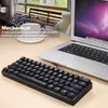 A mechanical keyboard and a laptop are placed on a wooden desk, with a window and a chair in the background. Podgląd zdjęcia produktu