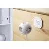 A white spherical power strip with multiple outlets is shown on a wooden surface next to a white wall-mounted light switch. Produktbild-Vorschau