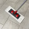 A mop with a microfiber pad and a telescopic handle is shown on a tiled floor. Produktbild-Vorschau