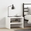 A white bedside table with a lamp, books, and a cup on it, next to a bed. Náhľad obrázku produktu