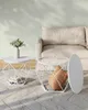 Two white geometric side tables on a rug next to a sofa. One table holds a vase with greenery and books, while the other has a cushion inside. Produktbild-Vorschau