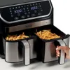 A close-up shot of a dual-basket air fryer filled with french fries, with a hand reaching to pull out one of the baskets. Podgląd zdjęcia produktu
