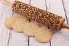 A wooden rolling pin with an engraved floral pattern lies next to several round cookies embossed with the same pattern. Produktbild-Vorschau