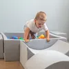 A young child is playing in a soft play area with colorful balls. Produktbild-Vorschau