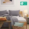 A neatly made bed with gray bedding, a bedside table with a lamp and a pitcher, and a basket with pillows. Produktbild-Vorschau