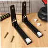 Two black metal brackets are shown on a wooden surface, with some accessories like screws and a foam grip nearby. A weight plate is visible in the background. Produktbild-Vorschau