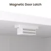 A close-up view of a magnetic door latch mechanism attached to the underside of a white cabinet or shelf. Produktbild-Vorschau