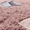 A close-up view of a fluffy pink rug with two gray slippers on it. Produktbild-Vorschau