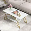 A white marble-patterned coffee table with gold metal legs and a lower shelf, placed on a light gray rug next to a sofa. Produktbild-Vorschau