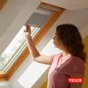 A young woman is adjusting a roller blind in a skylight window. Produktbild-Vorschau