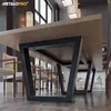 A long dining table with black trapezoidal legs, set in a modern dining room with chairs and decorative lighting. Produktbild-Vorschau