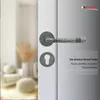 A close-up of a door handle and keyhole set on a white door, with a blurred interior scene in the background. Produktbild-Vorschau