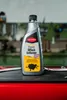 A bottle of Caramba Oelfleck Entferner is placed on a dark surface in a workshop setting. Produktbild-Vorschau