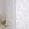 A close-up view of a white sheer curtain with a damask pattern, with a bouquet of white flowers to the left. Produktbild-Vorschau
