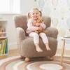 A young girl is sitting on a child-sized armchair holding a teddy bear. The room has a playful wallpaper with hot air balloons. Produktbild-Vorschau