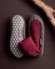 A pair of slippers and a sock laid out on a dark brown surface with a piece of wood in the upper right corner. Produktbild-Vorschau