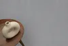 A beige donut-shaped vase sits on a round wooden table against a speckled gray background. Anteprima dell’immagine prodotto