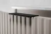 A close-up shot of a black shelf placed on top of a beige radiator. Anteprima dell’immagine prodotto