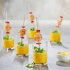 Several glasses of yellow soup with shrimp skewers on top, garnished with mint and red pepper pieces. Voir les images du produit