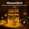 A glass jar filled with water and LED string lights, placed on an open book. Produktbild-Vorschau