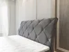A close-up view of a gray upholstered headboard and mattress of a bed. Produktbild-Vorschau