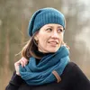 A woman wearing a teal knit hat and scarf outdoors. Produktbild-Vorschau