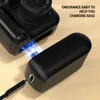 A black digital camera is shown with a black charging base, with blue electrical sparks indicating charging. Produktbild-Vorschau