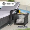 A gray polyrattan side table with a glass of yellow liquid and magazines on top, placed next to a lounge chair by a swimming pool. Anteprima dell’immagine prodotto