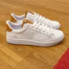 A pair of white K-Swiss sneakers with brown accents, placed on a wooden floor. Produktbild-Vorschau