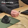 A person's hand is holding a USB cable near a vertical mouse on a desk. Produktbild-Vorschau