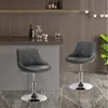 Two gray bar stools are shown in a modern kitchen or bar area, with a counter and shelving in the background. Náhľad obrázku produktu