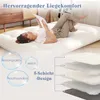 A woman is lying on a mattress, reading a book. The mattress is on the floor in a room. Produktbild-Vorschau