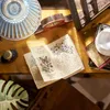A close-up view of a miniature book nook on a wooden surface, featuring a book, an inkwell, and decorative elements. Náhled obrázku produktu