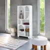 A white organic bookshelf with 8 compartments is shown in a modern room with concrete walls and large windows. Produktbild-Vorschau