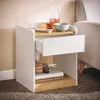A white and wood-tone nightstand next to a sofa, with items on top and on a shelf. Produktbild-Vorschau