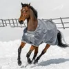 A brown horse wearing a gray turnout blanket runs through the snow, with a wooden fence in the background. Voir les images du produit