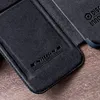 A close-up view of a dark gray leather phone case with embossed branding and text, resting on a wooden surface. Produktbild-Vorschau