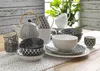 A collection of ceramic tableware, including bowls, cups, and a teapot, arranged on a table with a lace runner. Produktbild-Vorschau